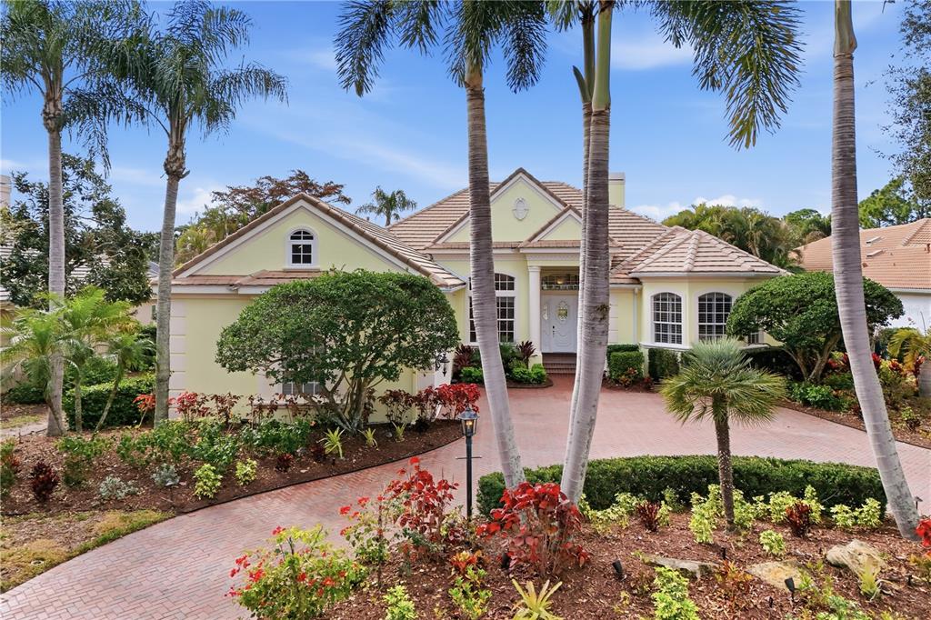 A pale yellow single-story house with a brick driveway and palm trees in the front — 7908 WARWICK GARDENS LANE, UNIVERSITY PARK, FL