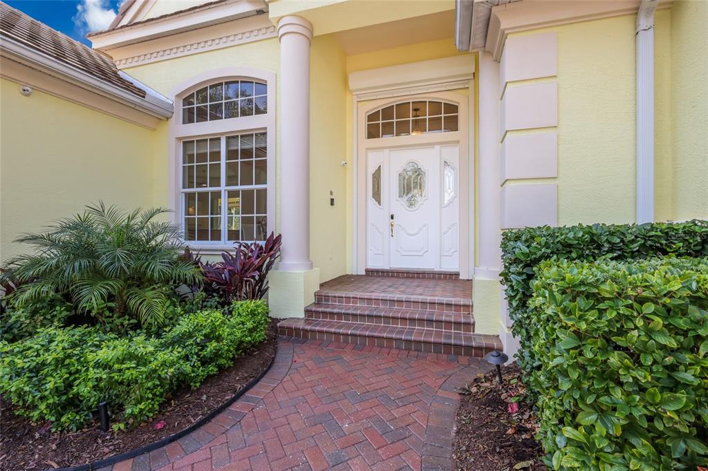 The exterior entrance features a brick walkway, three steps, a white door, and two columns — 7908 WARWICK GARDENS LANE, UNIVERSITY PARK, FL
