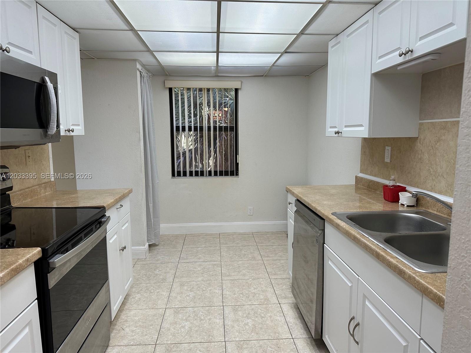 A galley kitchen features white cabinets, tan countertops, stainless steel appliances, and a drop ceiling — 400 Commodore Dr # 308, Plantation FL 33325, PLANTATION, FL