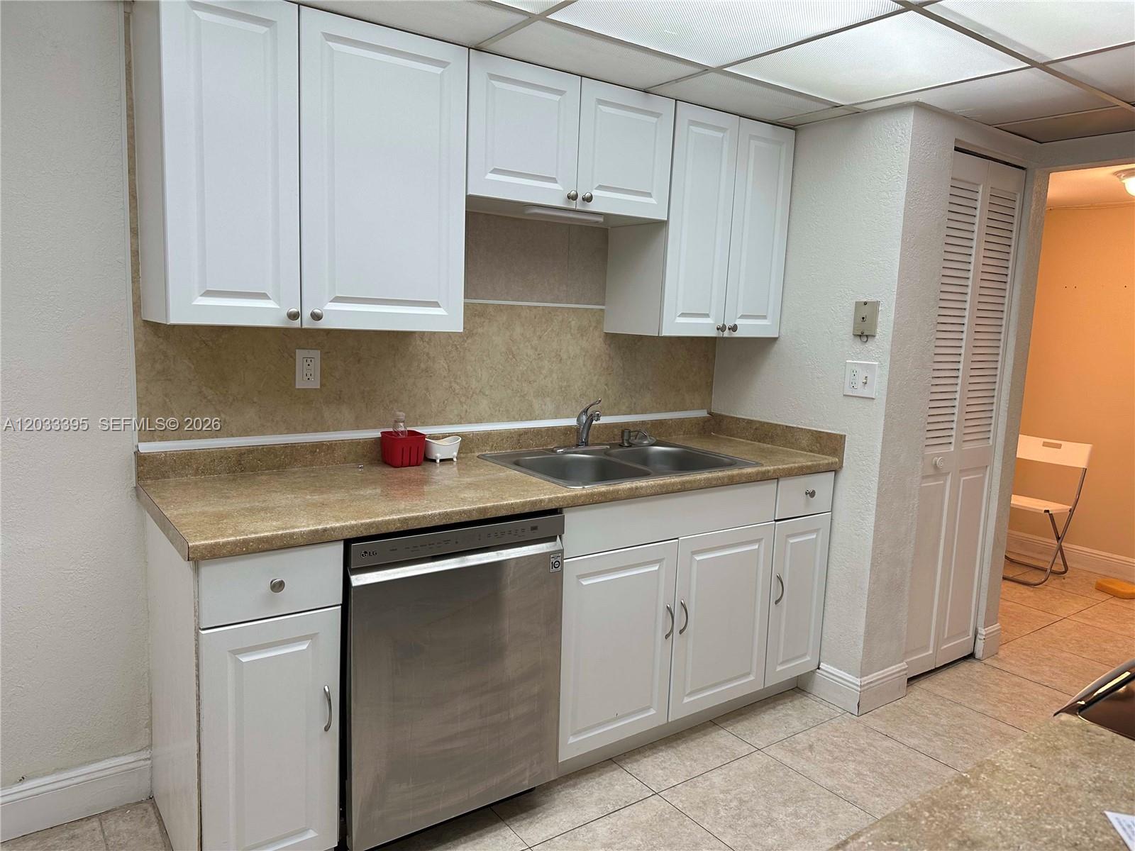 A kitchen features white cabinets, a stainless steel dishwasher, and tan laminate countertops — 400 Commodore Dr # 308, Plantation FL 33325, PLANTATION, FL