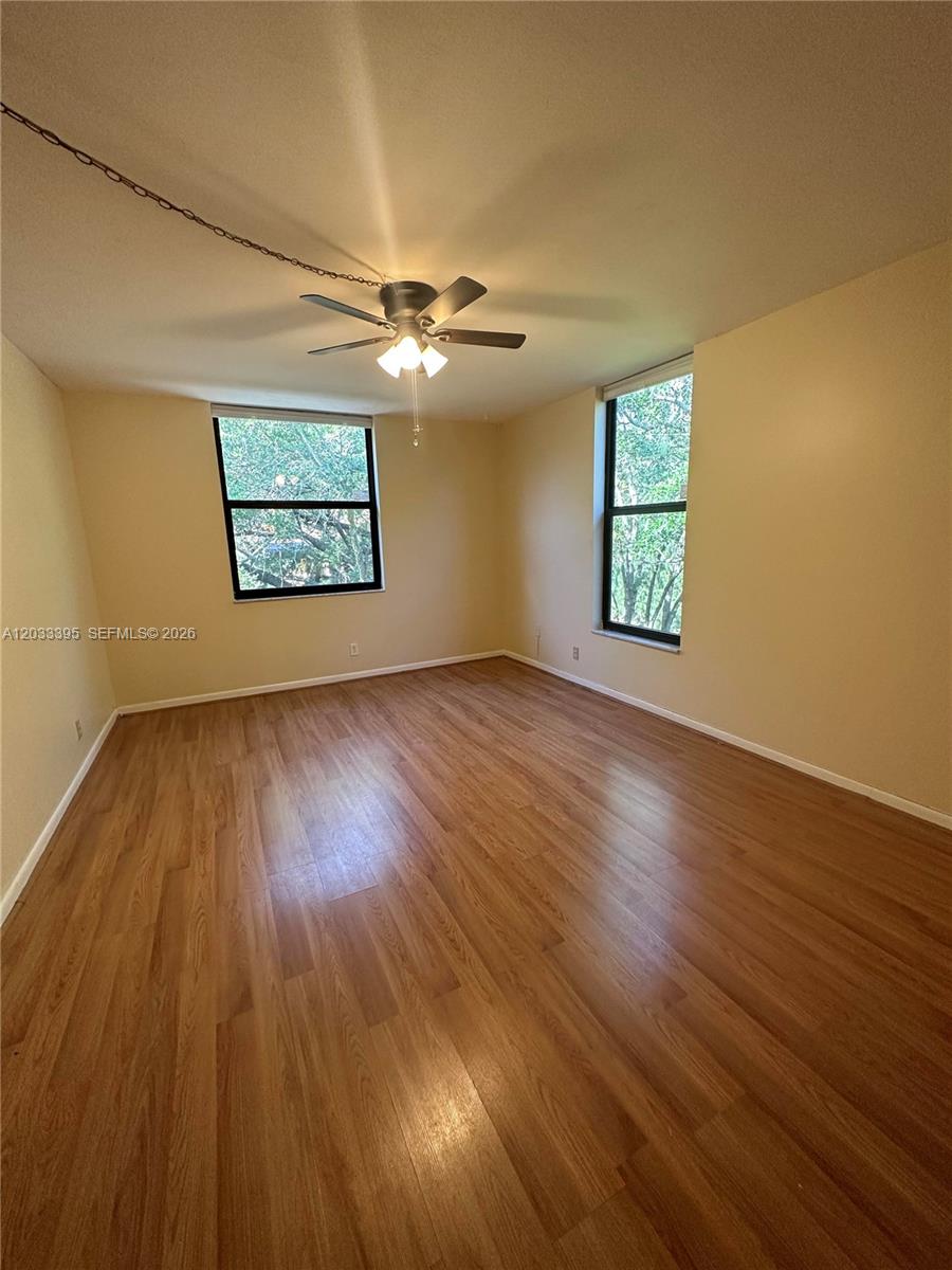 An empty room features light-colored walls, wood-look flooring, a ceiling fan, and two windows — 400 Commodore Dr # 308, Plantation FL 33325, PLANTATION, FL