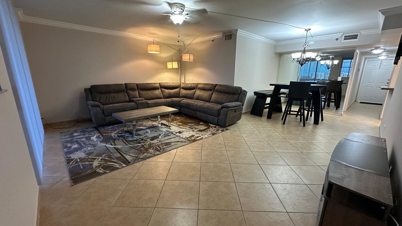 A living room with a gray sectional sofa, area rug, and an adjacent dining area — 3300 W Rolling Hills Circle # 708, Davie FL 33328, DAVIE, FL