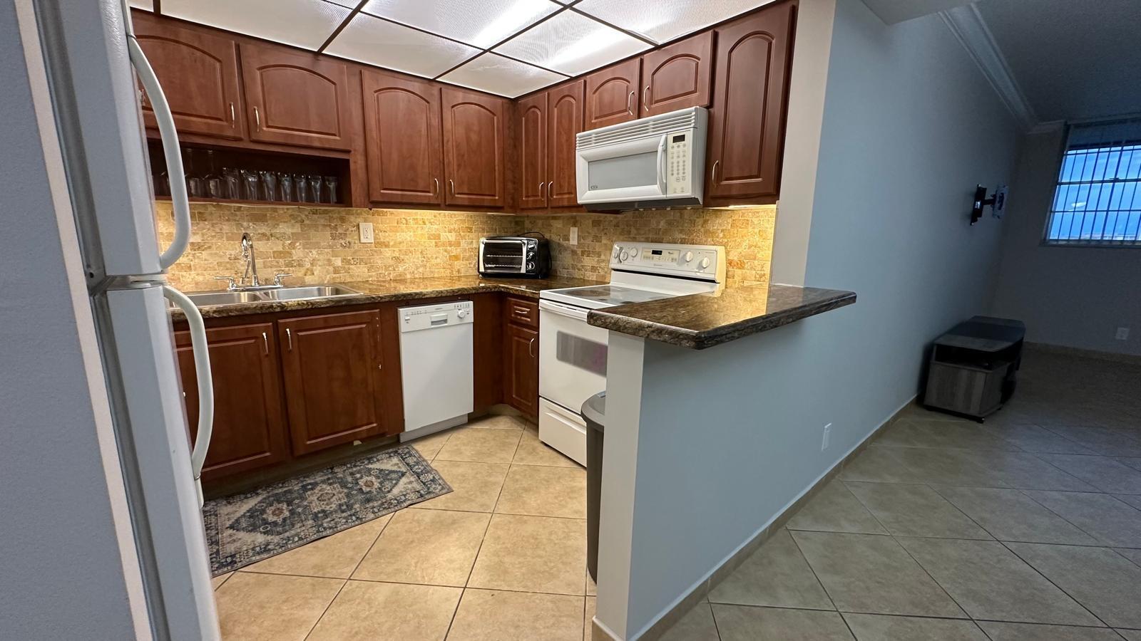 A kitchen features dark wood cabinets, granite countertops, a tiled backsplash, and white appliances — 3300 W Rolling Hills Circle # 708, Davie FL 33328, DAVIE, FL