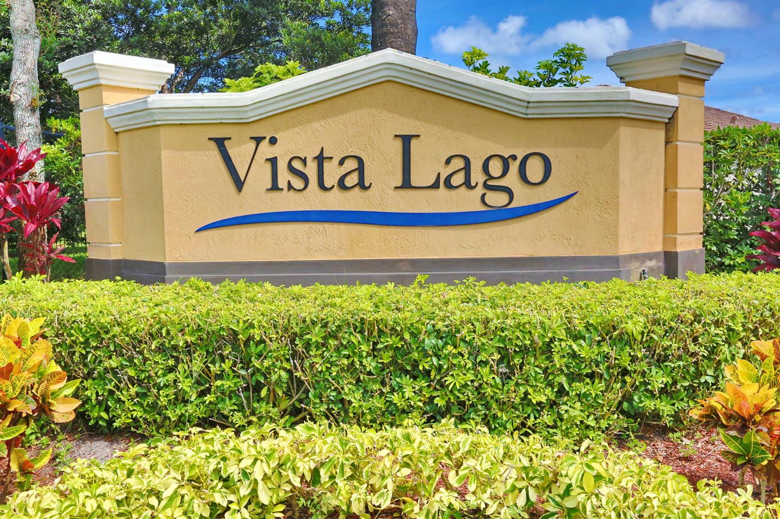 A beige monument sign with the text Vista Lago sits behind a manicured green hedge — 7171 Prudencia Drive, Lake Worth FL 33463, LAKE WORTH, FL