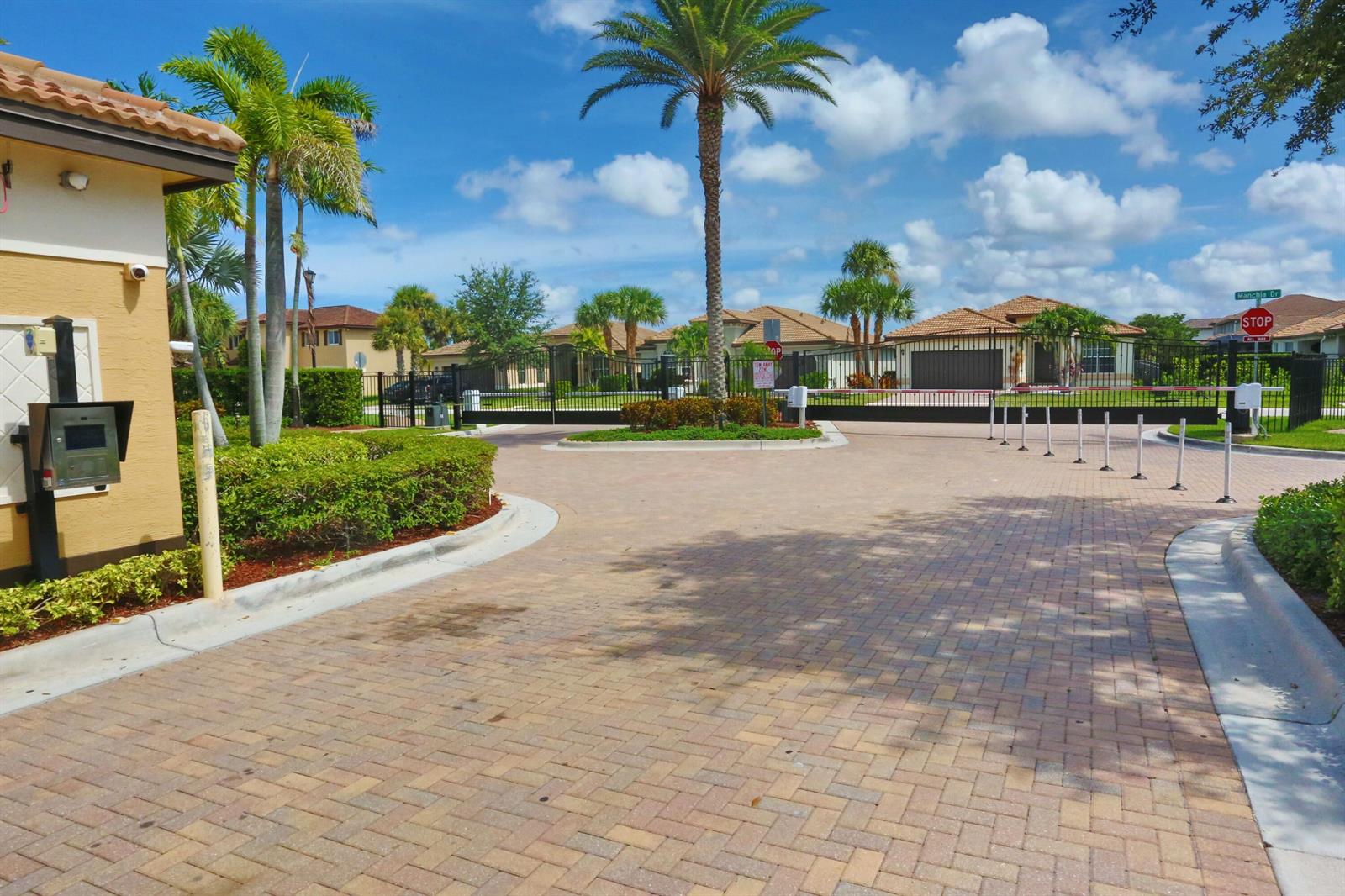 A gated entrance with a brick-paved driveway, palm trees, and a stop sign — 7171 Prudencia Drive, Lake Worth FL 33463, LAKE WORTH, FL