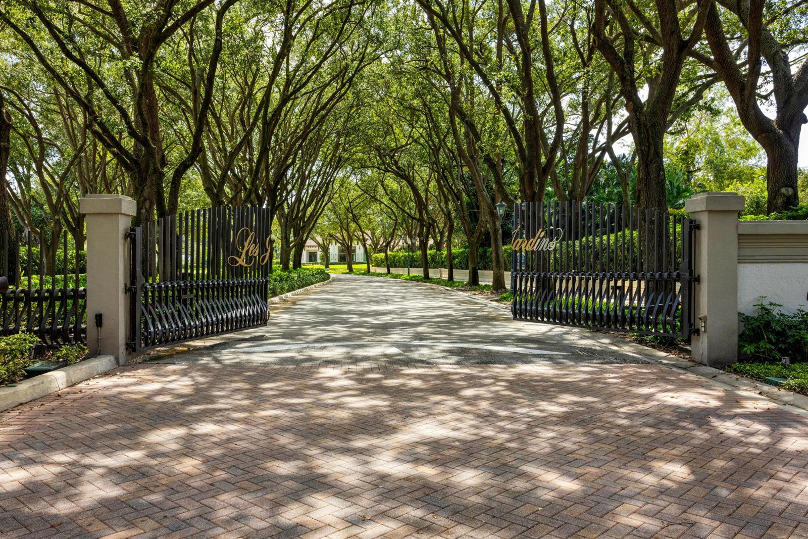 A paved driveway leads through an open metal gate flanked by large trees — 4600 NW 24th Way, Boca Raton FL 33431, BOCA RATON, FL