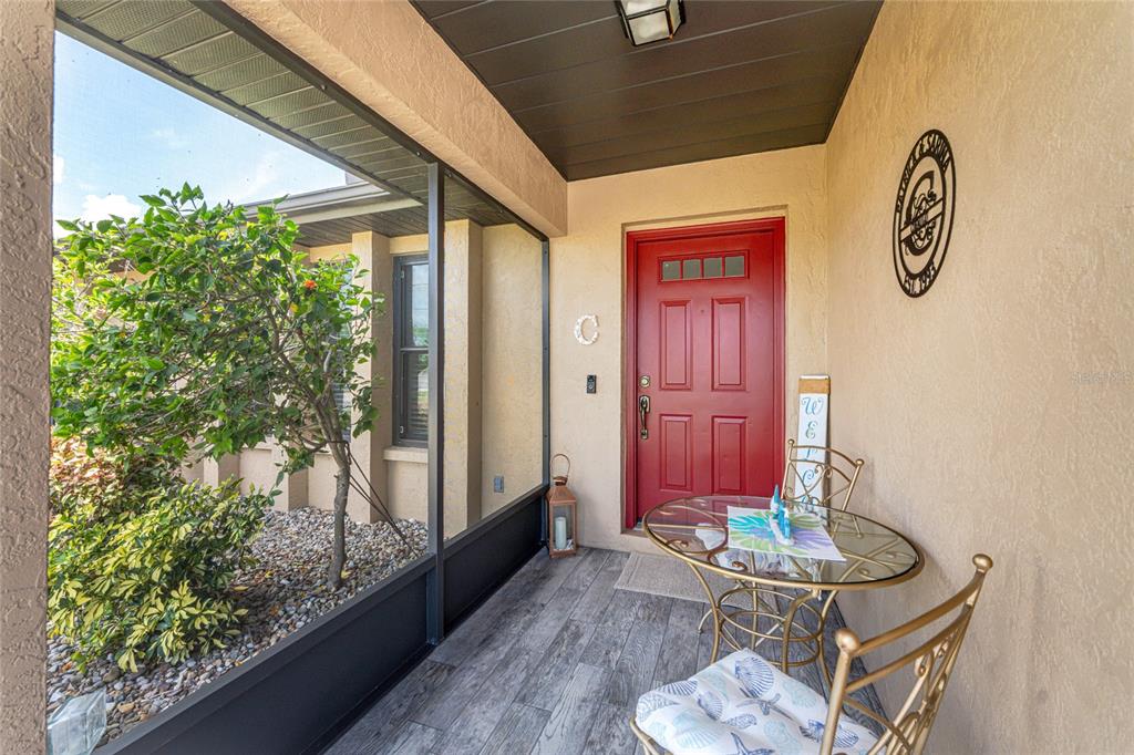A covered entryway features a red front door, a glass-topped table, and wood-look tile flooring — 255 MARK TWAIN LANE, ROTONDA WEST, FL