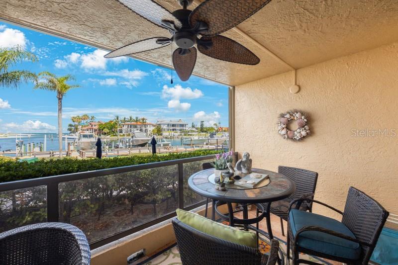A covered balcony features a ceiling fan, a small dining set, and a waterfront view — 1060 PINELLAS BAYWAY S UNIT 103, ST PETERSBURG, FL
