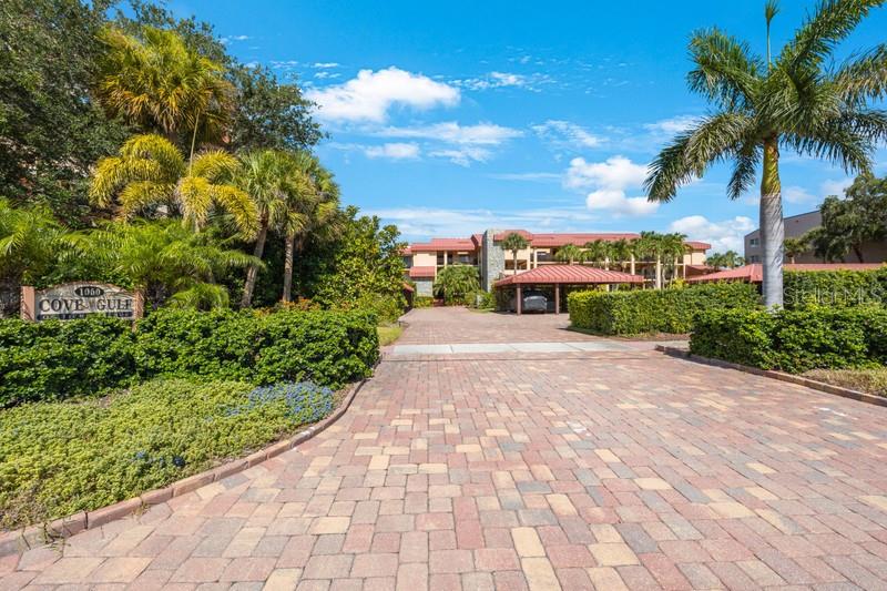 A paved driveway leads toward a multi-story apartment building with a covered parking area — 1060 PINELLAS BAYWAY S UNIT 103, ST PETERSBURG, FL