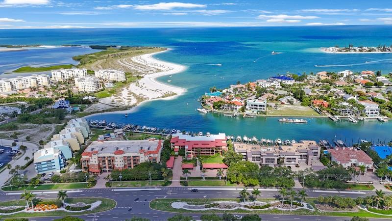 An aerial view shows a coastal residential area with buildings, a marina, and a sandy beach — 1060 PINELLAS BAYWAY S UNIT 103, ST PETERSBURG, FL