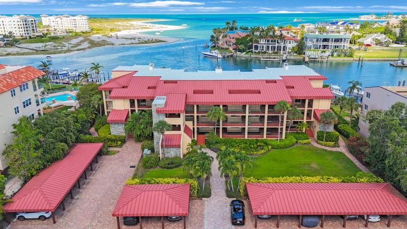 An aerial view shows a multi-story apartment building with a red roof near water — 1060 PINELLAS BAYWAY S UNIT 103, ST PETERSBURG, FL