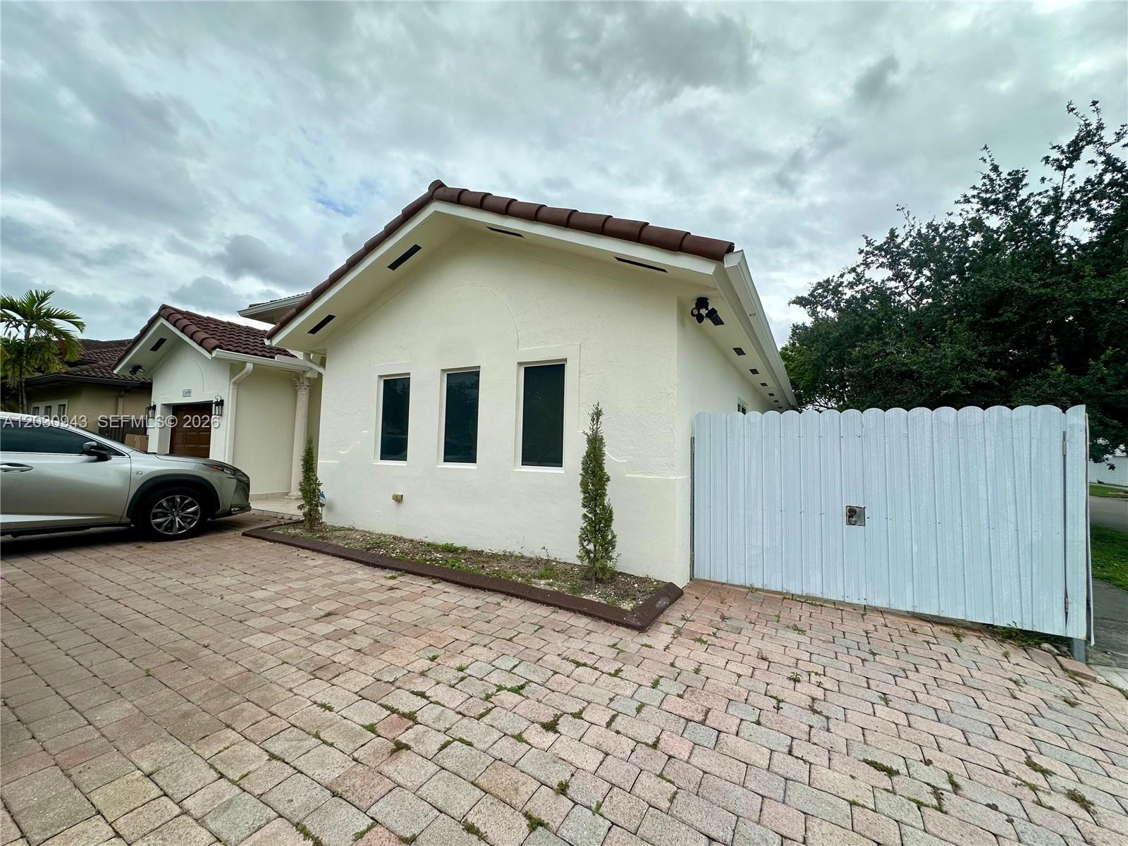 A paved driveway leads to a white house with three windows and a wooden gate — 15490 SW 10th St, Miami FL 33194, MIAMI, FL