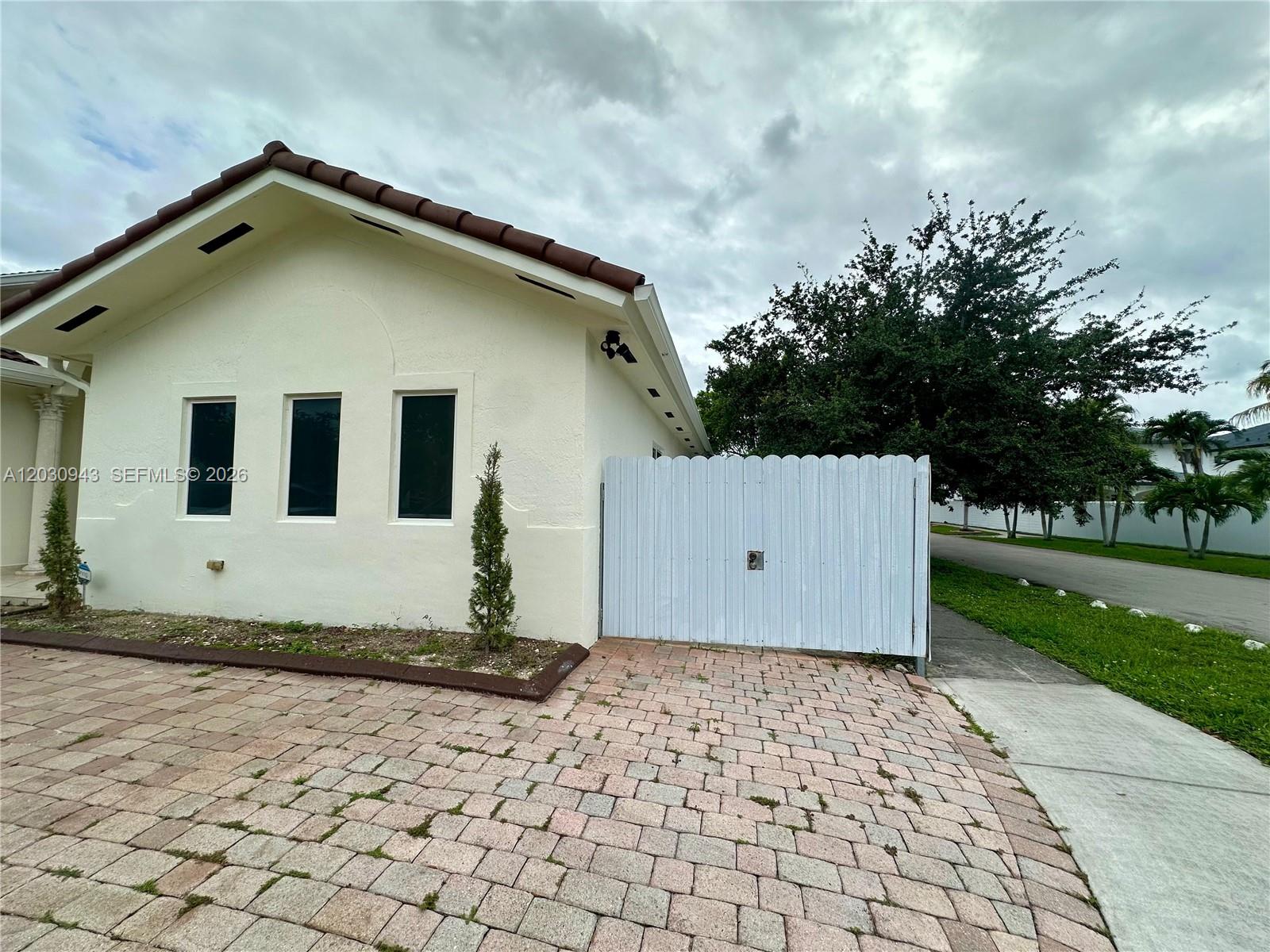 A light-colored house with a tiled roof and a white fence sits beside a driveway — 15490 SW 10th St, Miami FL 33194, MIAMI, FL