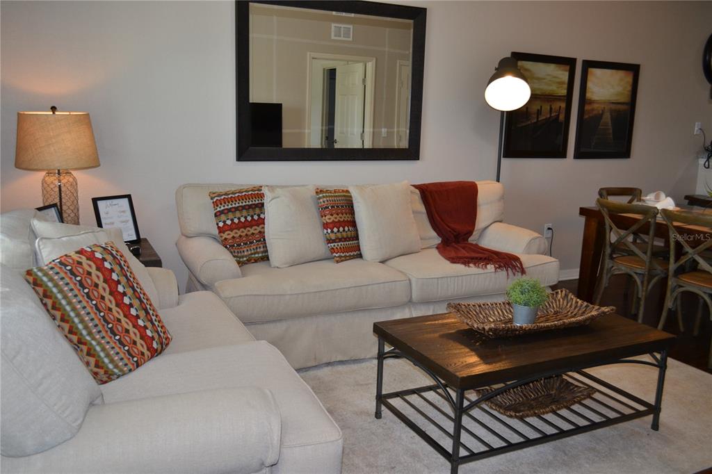 A living room features two beige sofas, a wooden coffee table, and a large mirror — 3208 CUPID PLACE, KISSIMMEE, FL