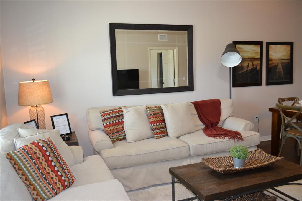 A living room features a beige sofa, a coffee table, a mirror, and a floor lamp — 3208 CUPID PLACE, KISSIMMEE, FL