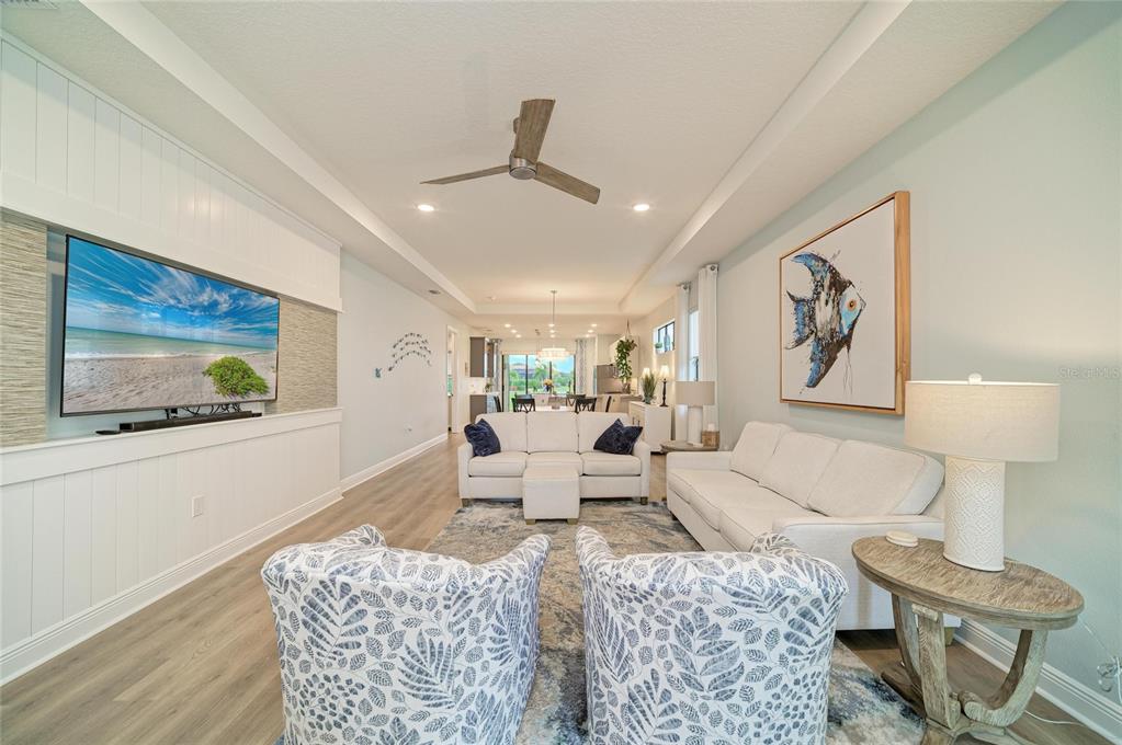 A bright living room features a wall-mounted television, white sofas, and patterned armchairs — 5286 BARNETT CIRCLE, BRADENTON, FL