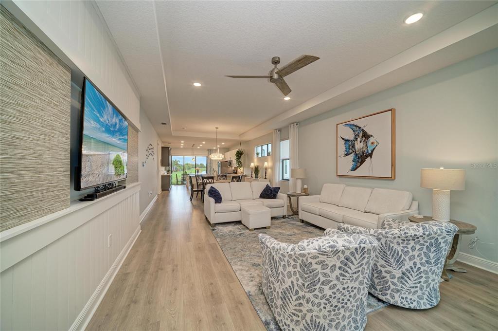 A living room with light wood floors, white sofas, patterned armchairs, and a wall-mounted television — 5286 BARNETT CIRCLE, BRADENTON, FL