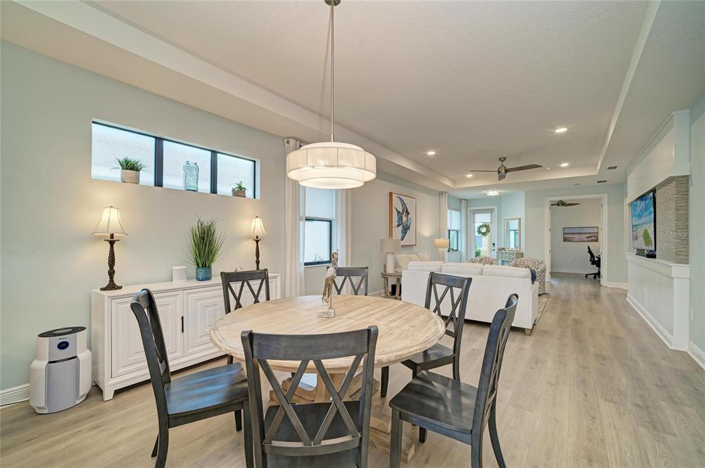 A dining area with a round wooden table and chairs sits before an open living room — 5286 BARNETT CIRCLE, BRADENTON, FL