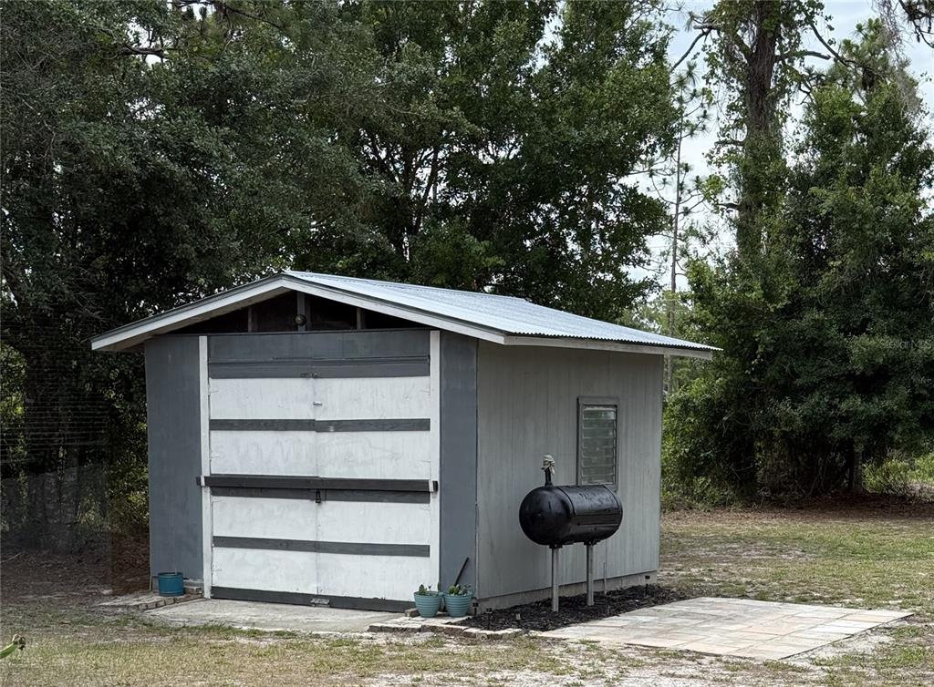 A gray shed with a metal roof and a large black grill sits outdoors — 3681 GARDENIA DRIVE, INDIAN LAKE ESTATES, FL