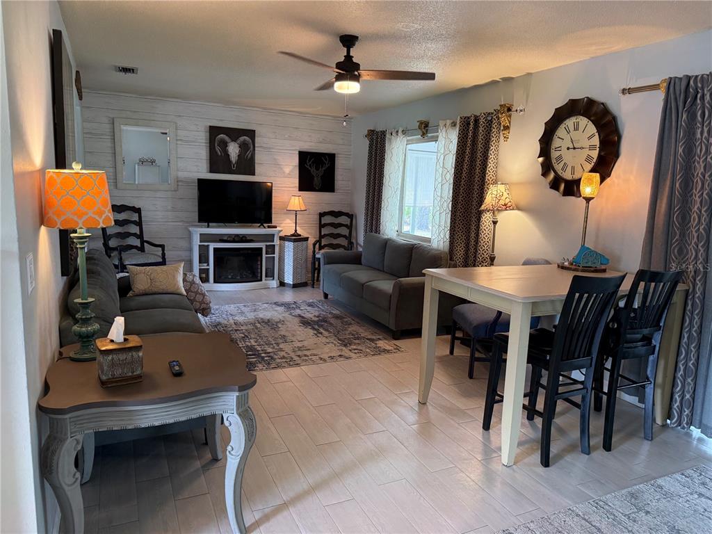 A living and dining room features wood-look tile floors, a fireplace, and a ceiling fan — 3681 GARDENIA DRIVE, INDIAN LAKE ESTATES, FL