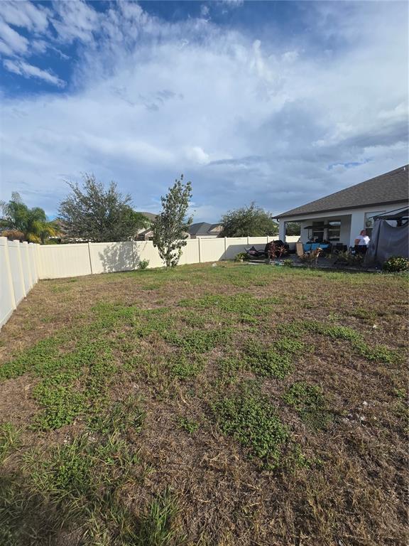 A view of a fenced backyard with sparse grass and a covered patio area — 11436 CHILLY WATER COURT, RIVERVIEW, FL