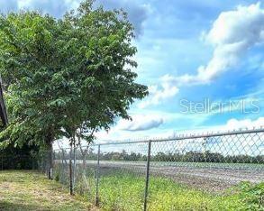 A chain-link fence separates a grassy yard from a large, open agricultural field — 3617 TOM BRYAN LANE, LAKELAND, FL