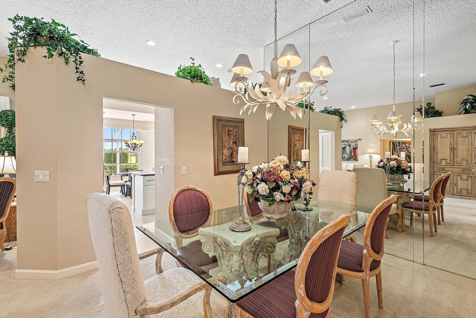 A dining room features a glass-topped table, upholstered chairs, a chandelier, and a mirrored wall — 240 Eagleton Estate Boulevard, Palm Beach Gardens FL 33418, PALM BEACH GARDENS, FL