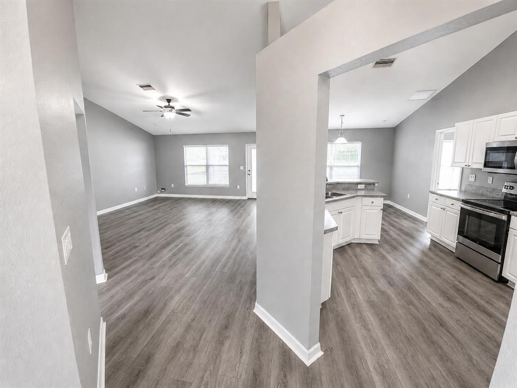 An open-concept living area and kitchen feature gray walls, white cabinets, and wood-look flooring — 3011 SHAWNEE TER, NORTH PORT, FL