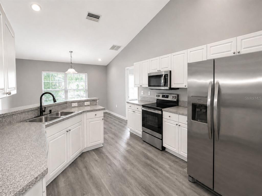 A kitchen features white cabinets, stainless steel appliances, grey countertops, and light wood-look flooring — 3011 SHAWNEE TER, NORTH PORT, FL
