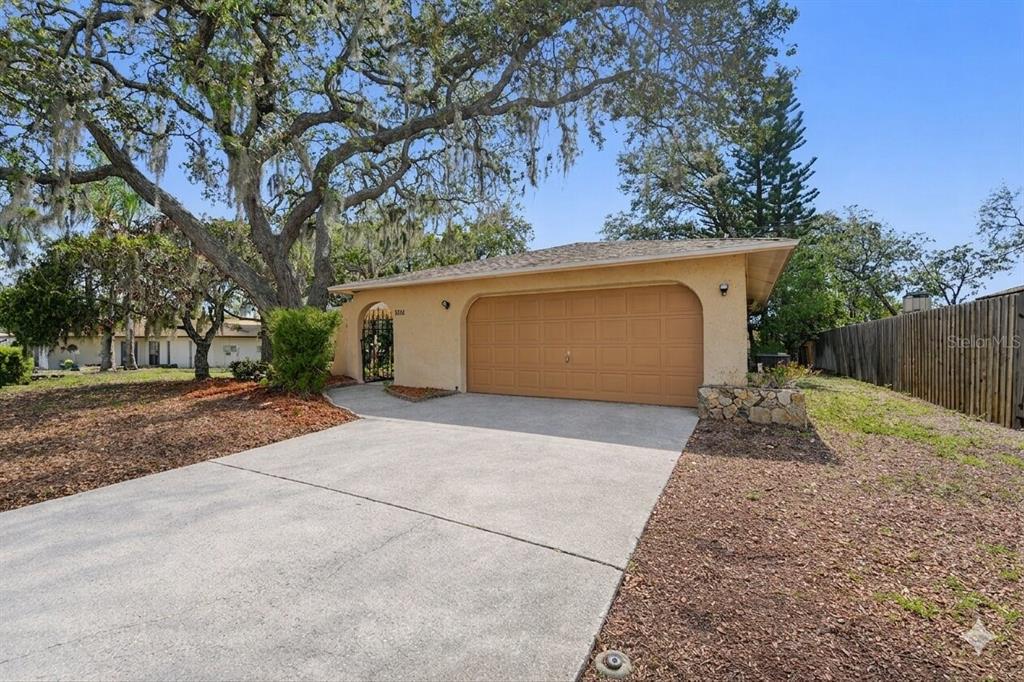 A single-story house with a tan stucco exterior, a two-car garage, and a concrete driveway — 8741 ELM LEAF COURT, PORT RICHEY, FL