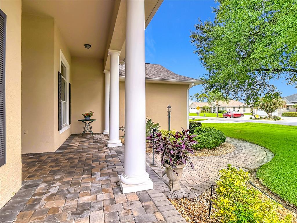 A covered porch features stone pavers, white columns, and a view of a suburban street — 5056 MYRTLE BEACH DRIVE, SEBRING, FL