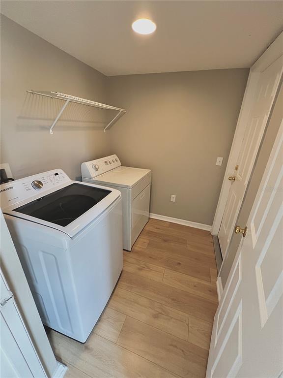 A laundry room featuring a washer, dryer, white wire shelving, and light wood-look flooring — 1418 SARASOTA DRIVE, KISSIMMEE, FL