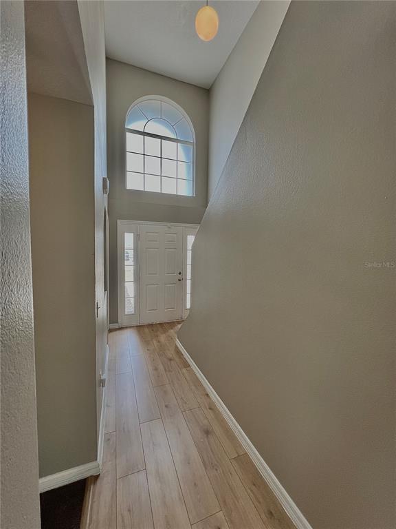 A foyer with light wood-look flooring, a tall arched window, and a white front door — 1418 SARASOTA DRIVE, KISSIMMEE, FL
