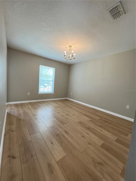 An empty room features light wood-look flooring, beige walls, a single window, and a chandelier — 1418 SARASOTA DRIVE, KISSIMMEE, FL