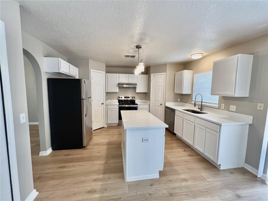 A kitchen features white cabinets, stainless steel appliances, a center island, and light wood flooring — 1418 SARASOTA DRIVE, KISSIMMEE, FL