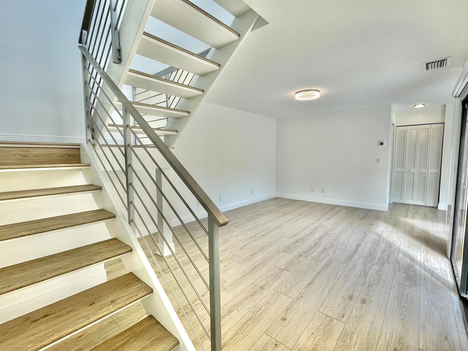 A modern living room features light wood-look flooring and a staircase with metal railings — 359 Prestwick Circle # 2, Palm Beach Gardens FL 33418, PALM BEACH GARDENS, FL