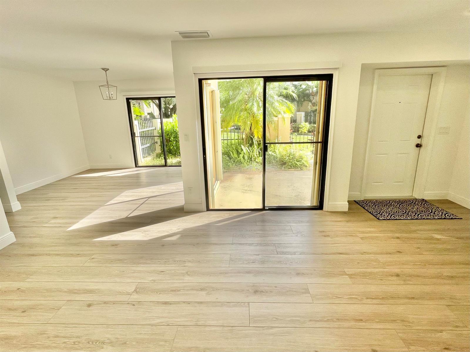 An open living area with light wood-look flooring, white walls, and two sliding glass doors — 359 Prestwick Circle # 2, Palm Beach Gardens FL 33418, PALM BEACH GARDENS, FL
