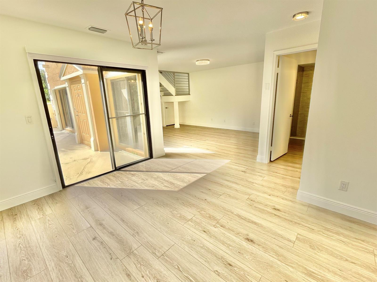 A bright room with light wood-look flooring, a hanging lantern fixture, and sliding glass doors — 359 Prestwick Circle # 2, Palm Beach Gardens FL 33418, PALM BEACH GARDENS, FL