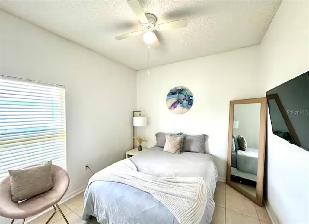 A bedroom features a bed, a ceiling fan, a floor mirror, and a wall-mounted television — 5212 JASMINE TRACE LANE, KISSIMMEE, FL