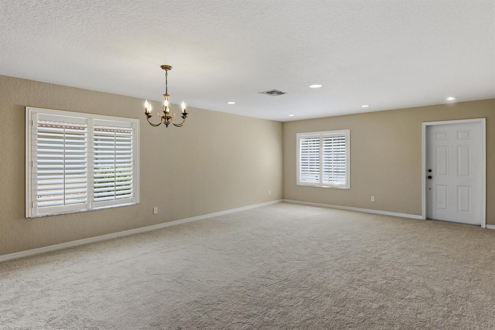 An empty room features beige walls, wall-to-wall carpeting, a chandelier, and white plantation shutters — 2020 SW Newport Isles Boulevard, FL 34953, FL