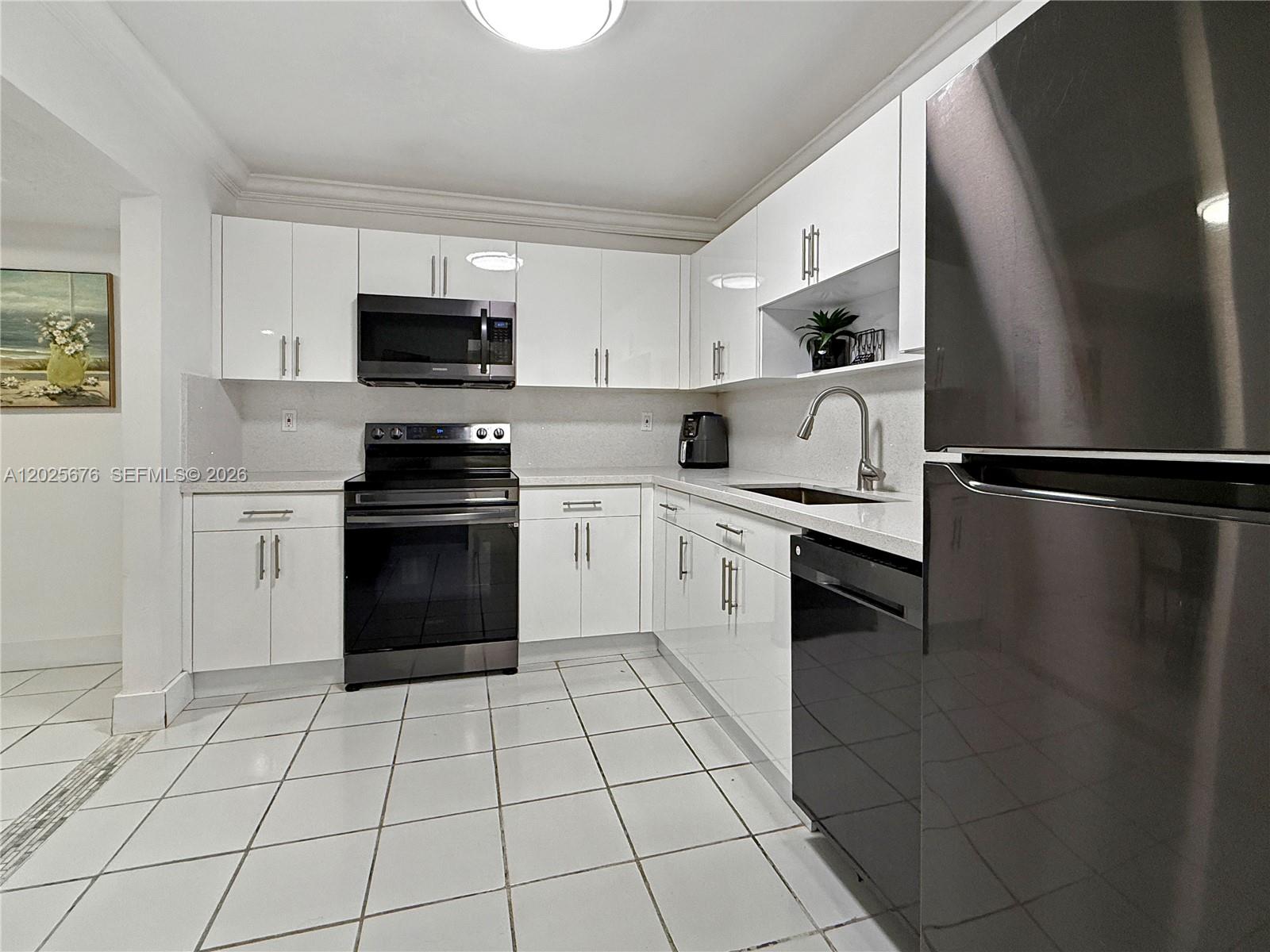 A kitchen features white cabinets, black appliances, light countertops, and white tile flooring — 9735 NW 52nd St # 209, Doral FL 33178, DORAL, FL