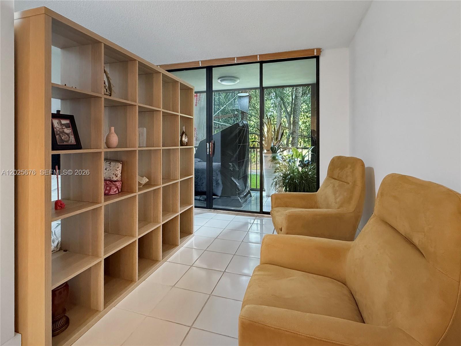 A room features a large wooden shelving unit, two yellow armchairs, and a sliding glass door — 9735 NW 52nd St # 209, Doral FL 33178, DORAL, FL