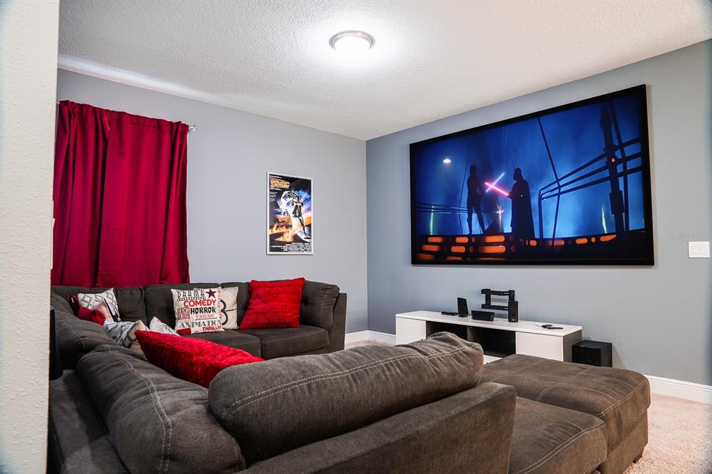 A home theater room features a large wall-mounted screen, a sectional sofa, and red curtains — 351 PENDANT COURT, KISSIMMEE, FL