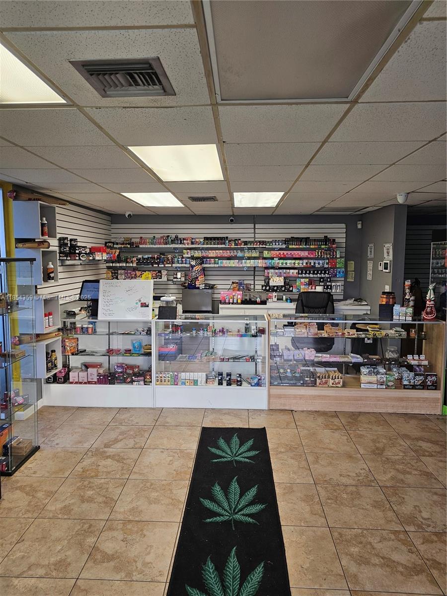 A retail shop interior features glass display cases, wall-mounted shelving, and a cannabis-themed floor mat — 510 s state RD 7, Plantation FL 33317, PLANTATION, FL