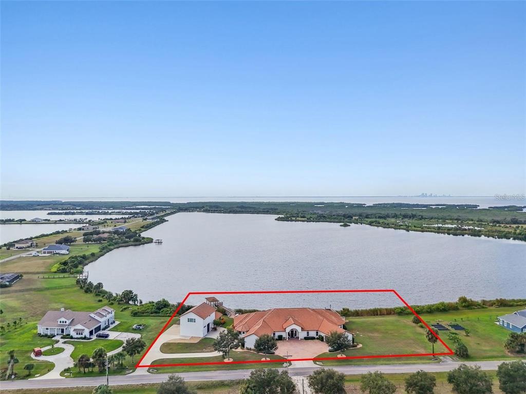 An aerial view shows a house with a red roof and a dock on a lake — 3215 GULF CITY ROAD, RUSKIN, FL