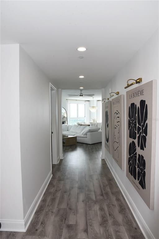A hallway with wood-look flooring leads to a living room with a white sectional sofa — 241 RIVERSIDE DRIVE UNIT 2009, HOLLY HILL, FL