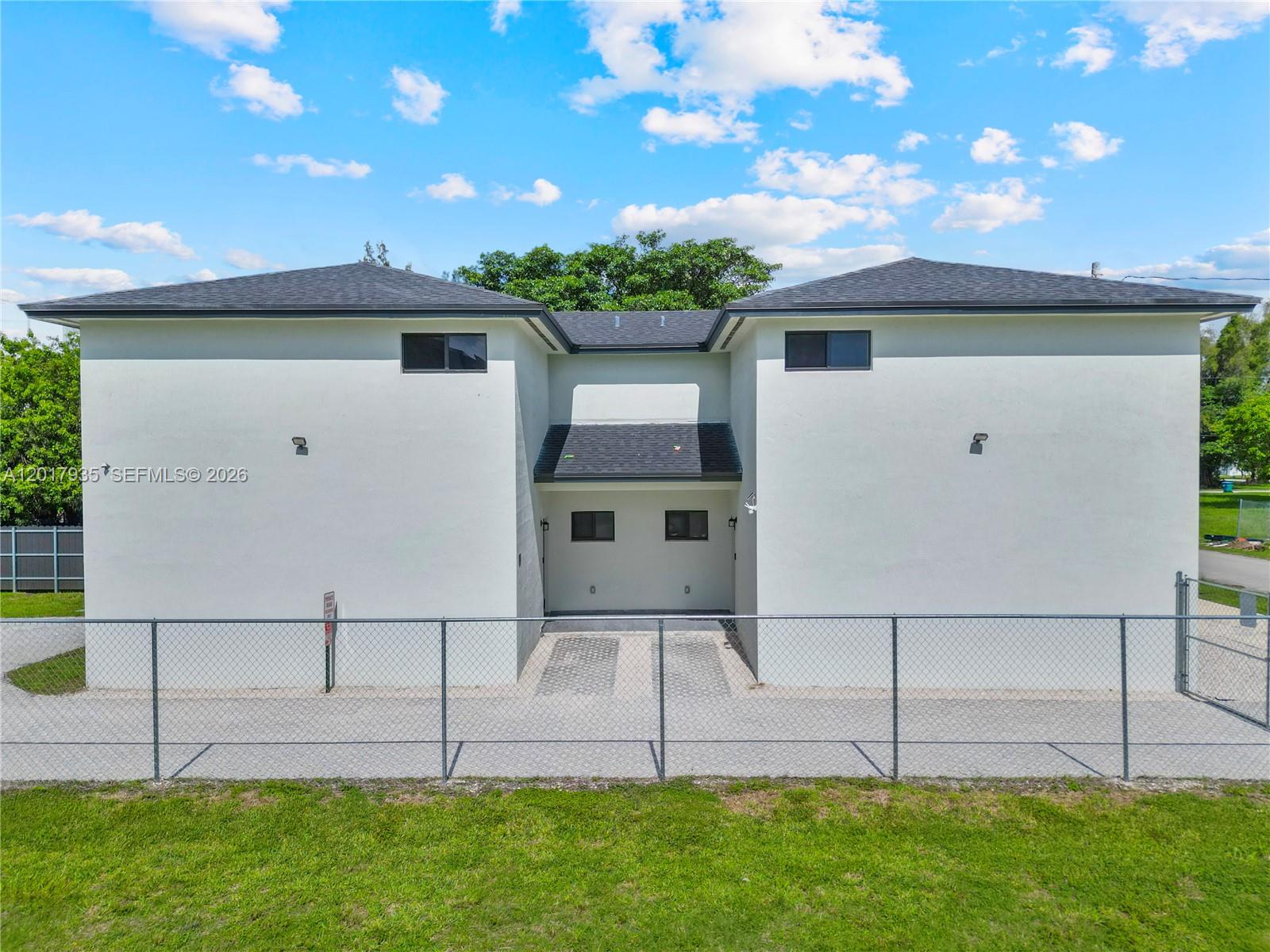 A two-story white building with a dark shingled roof stands behind a chain-link fence — 11970 SW 215th St # B, Miami FL 33177, MIAMI, FL
