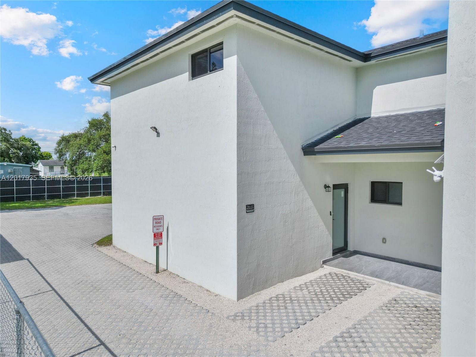 An exterior view of a white building with a paved driveway and a private road sign — 11970 SW 215th St # B, Miami FL 33177, MIAMI, FL