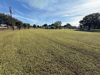 A wide, grassy vacant lot under a blue sky with trees and distant houses — 1063 Louisiana Avenue, Clewiston FL 33440, CLEWISTON, FL