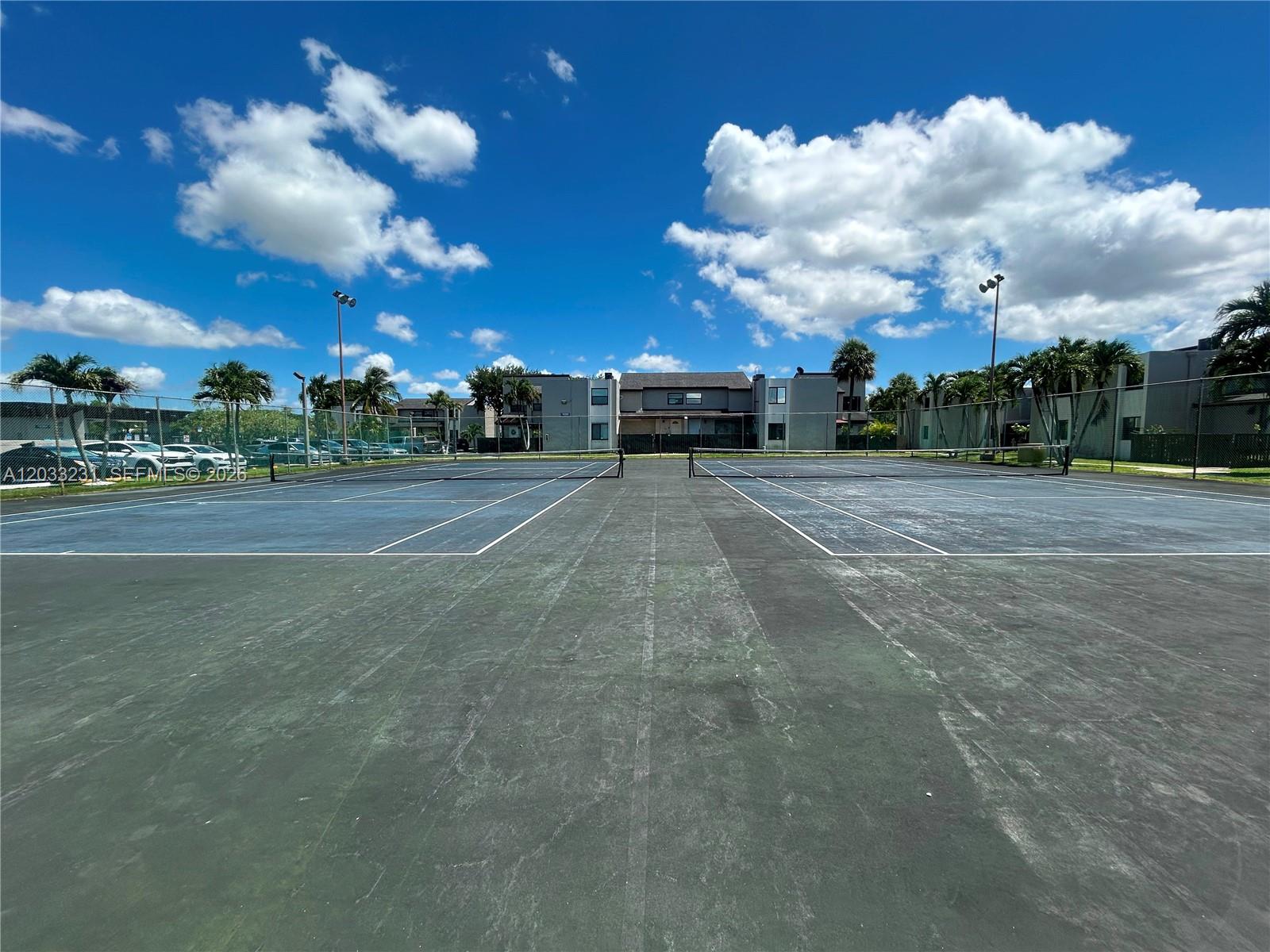 Two outdoor tennis courts with dark surfaces are enclosed by chain-link fencing under a blue sky — 10284 NW 9th St Cir # 204, Miami FL 33172, MIAMI, FL